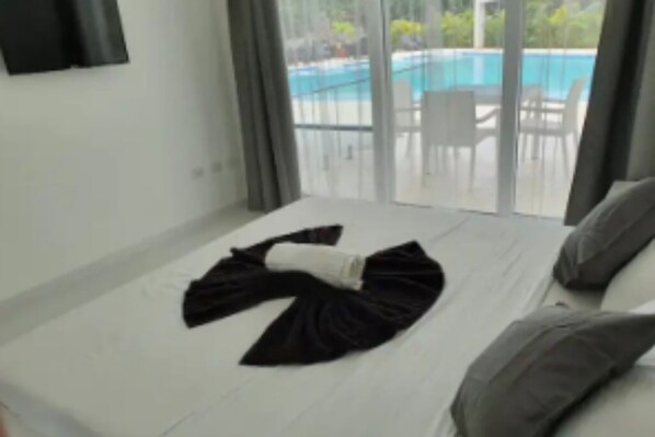 A hotel room with a bed, a view of a swimming pool, and a balcony with chairs.