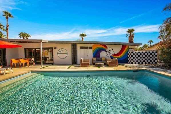 A modern house with a swimming pool, a mural, and outdoor furniture.