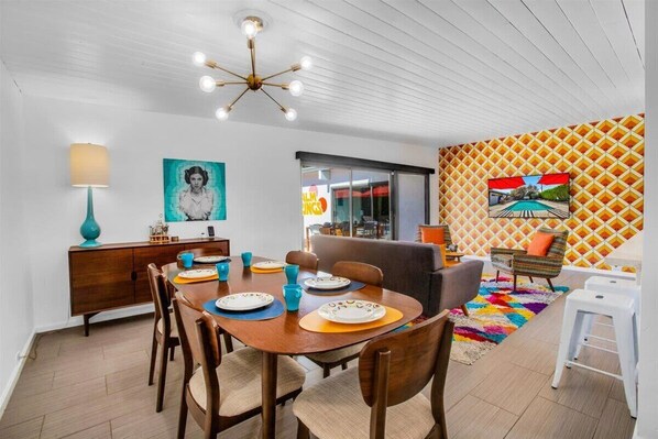A dining area with a wooden table, chairs, a chandelier, and a colorful wall mural.