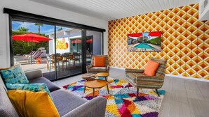 A modern living room with a sofa, armchairs, a colorful rug, and a large window overlooking a pool area.