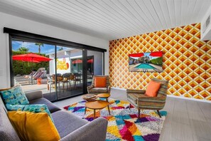 A modern living room with a sofa, armchairs, a colorful rug, and a large window overlooking a pool area.