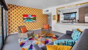 A modern living room with a patterned wall, a sofa, two armchairs, a coffee table, and a kitchen area with a refrigerator and sink.