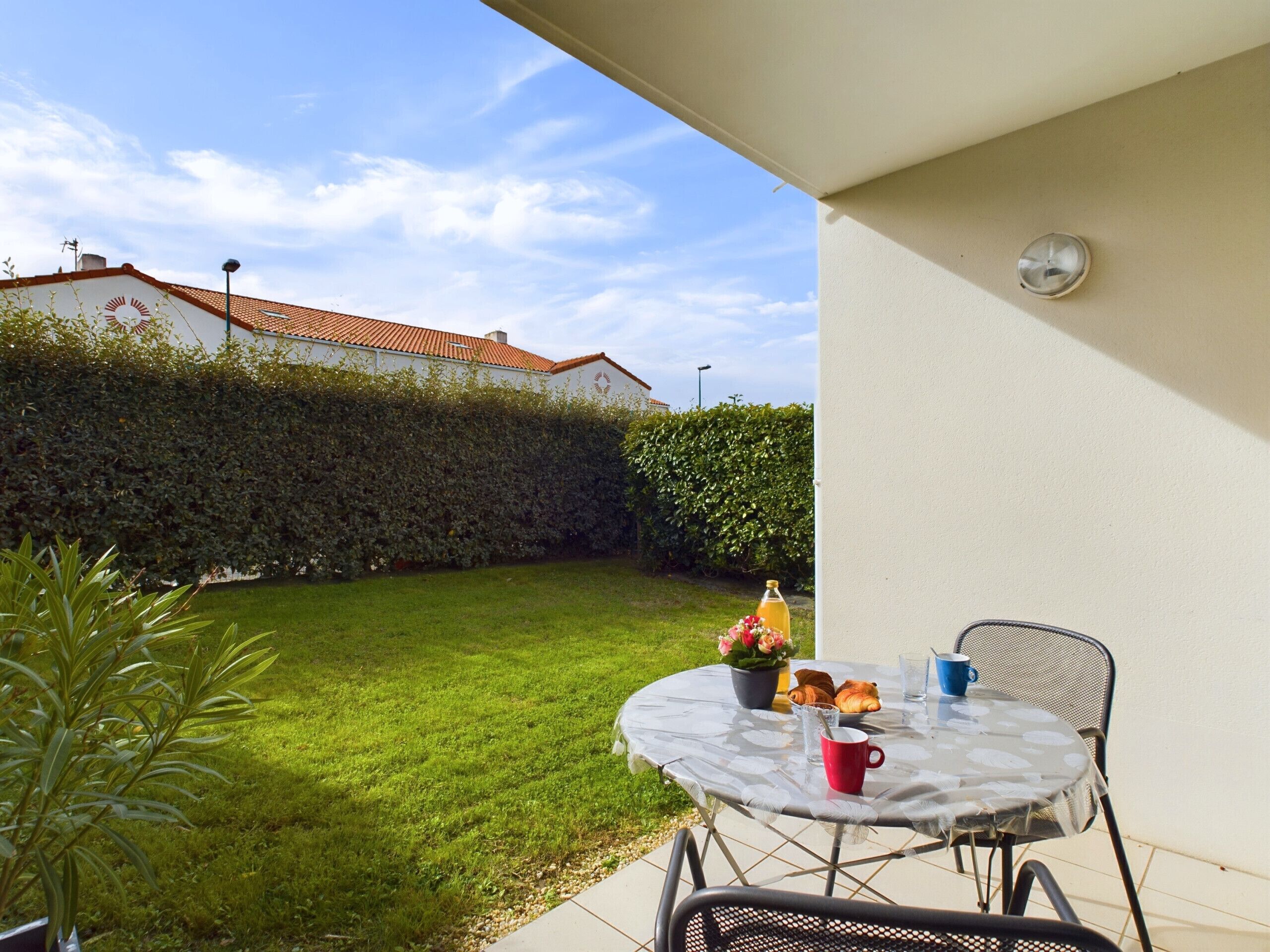 Une terrasse avec une table, des chaises et un petit espace jardin agrémenté d’une haie et de pelouse.