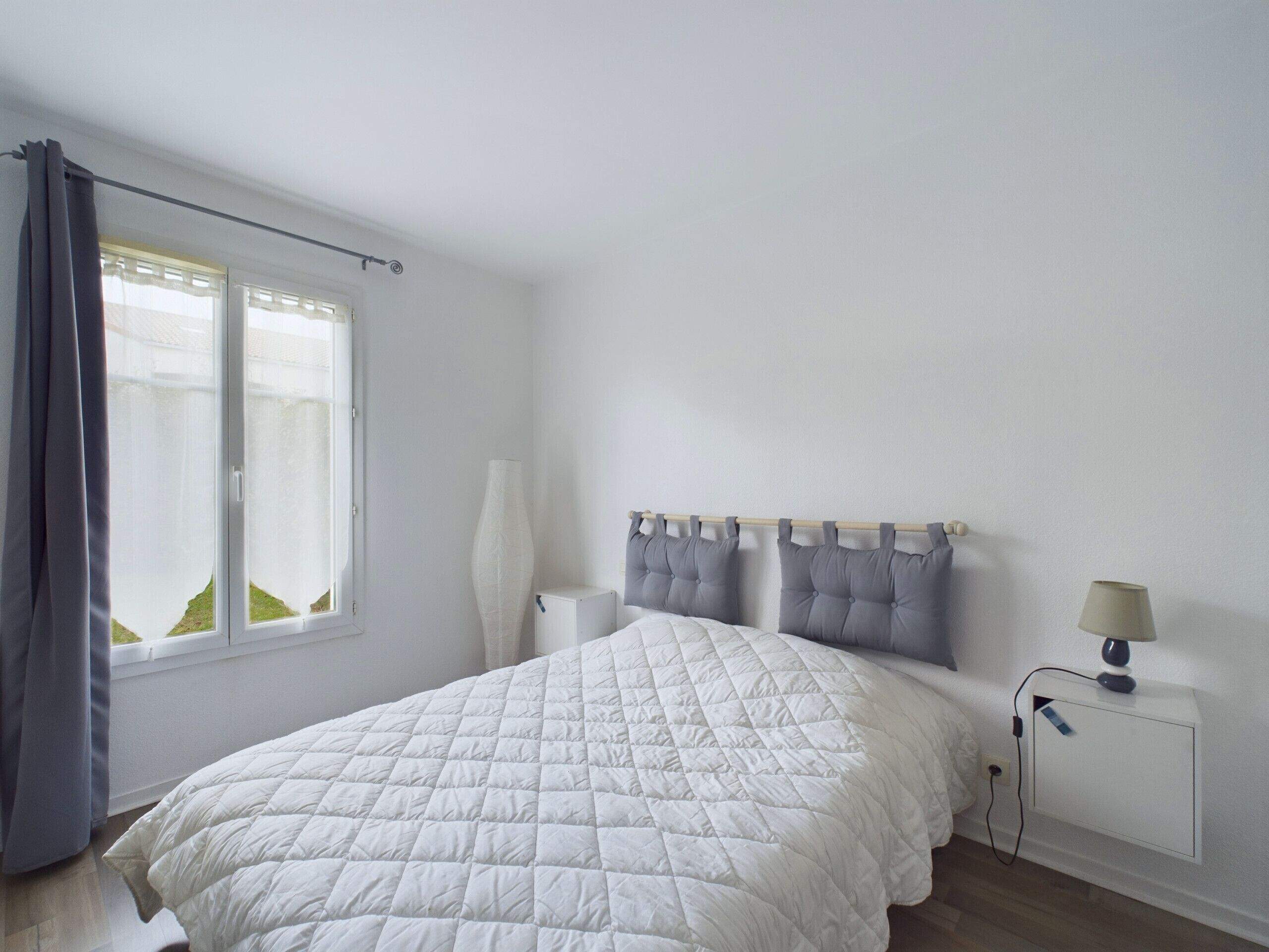 Une chambre à coucher avec un grand lit, une table de chevet avec une lampe, une fenêtre avec des rideaux et un radiateur.