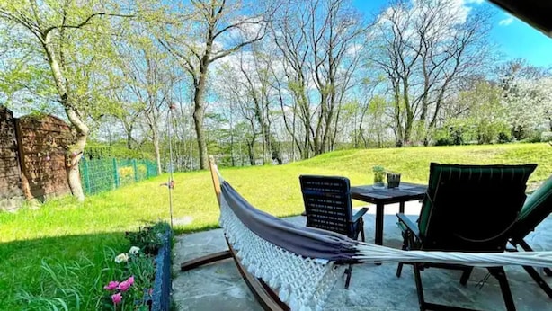 A hammock set up on a patio with a view of a grassy area and trees.