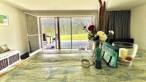 A room with a large sliding glass door leading to a balcony, a green vase with flowers, a small table with a candle, and a chair.