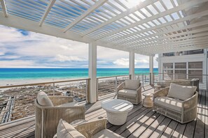 A covered outdoor area with wicker furniture and a view of the beach.