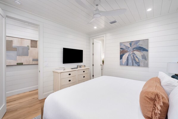 A bedroom with a bed, a dresser, a television, and a painting on the wall.