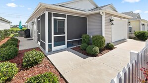Ein modernes eingeschossiges Haus mit überdachter Terrasse, Garage und gepflegtem Vorgarten mit Sträuchern und Mulch.