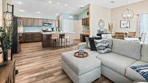Ein modernes Wohnzimmer mit grauem Sofa, Holzboden und einer Küche im Hintergrund.