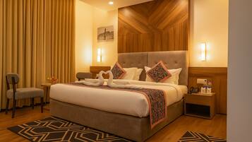 Habitación de hotel con una cama grande, dos mesitas de noche, una silla, un escritorio y una lámpara de pared.