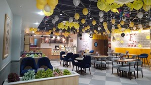 A restaurant interior with yellow and white balloons, a counter with flowers, and a pizza sign. - Hotel Luxurio (Amritsar)