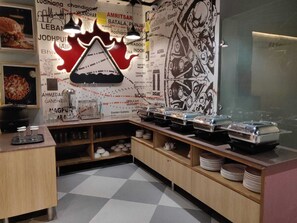 A kitchen area with a counter, shelves, and a wall with various text and graphics. - Hotel Luxurio (Amritsar)