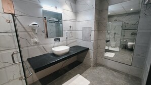 A modern bathroom with a marble-tiled wall, a white sink, a glass shower enclosure, and a towel rack. - Hotel Luxurio (Amritsar)