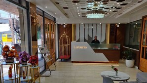 A modern hotel lobby with a reception desk labeled 'Luxurio', a chandelier, and a reception area with a receptionist. - Hotel Luxurio (Amritsar)