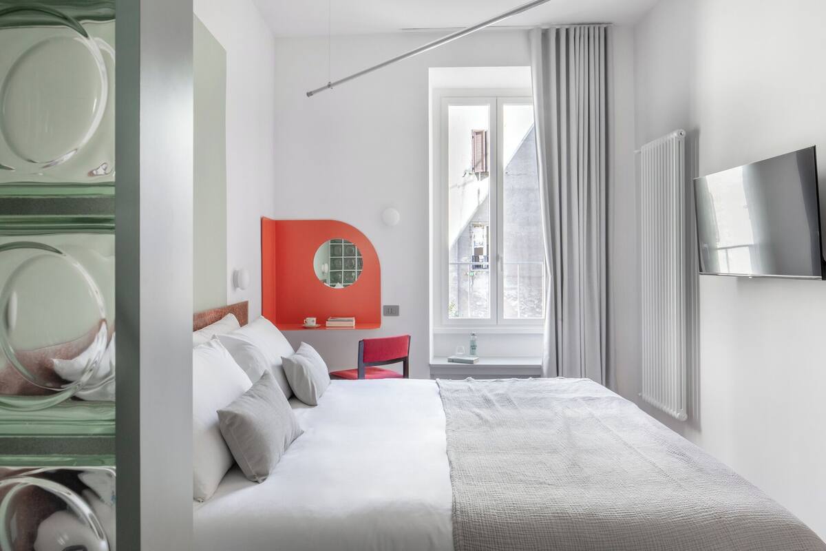 Een moderne hotelkamer met een bed, een televisie, een raam met gordijnen en uitzicht op de straat.