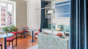Cozinha moderna com armários azuis, uma mesa redonda e cadeiras. Há uma janela com vista para prédios.