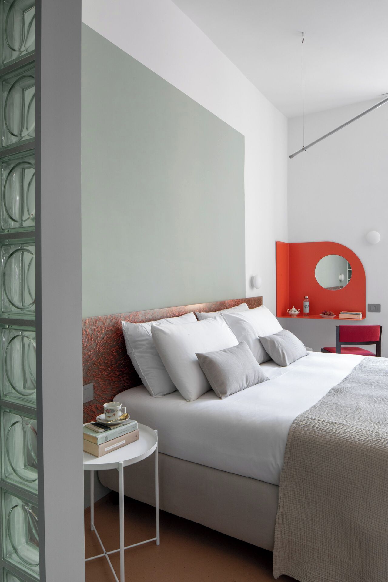 A modern bedroom with a bed, bedside table, and a red-framed mirror.
