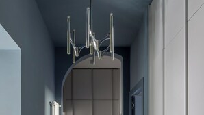 Um corredor estreito com um elevador moderno, um radiador e uma pequena planta numa prateleira.
