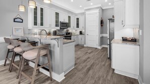 Une cuisine moderne avec des meubles blancs, un îlot central doté de tabourets et des luminaires suspendus.
