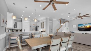 Une cuisine moderne avec des meubles blancs, un coin repas doté d’une table et de chaises en bois, et un ventilateur de plafond.
