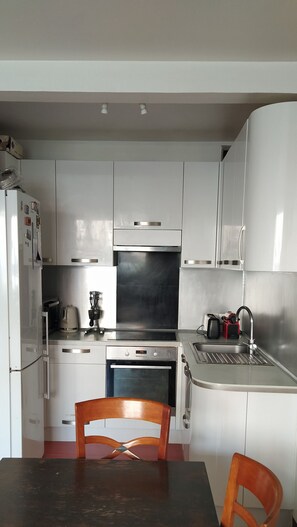 Compact kitchen with refrigerator, microwave, oven, and sink, plus a dining area with two chairs.