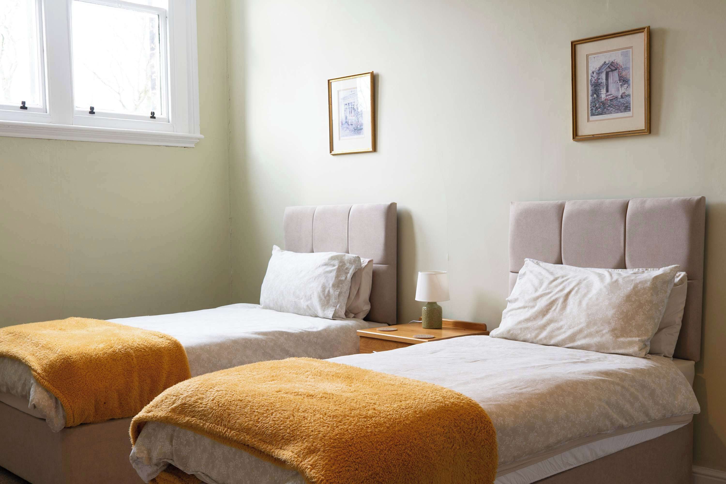 A hotel room with two beds, each with a headboard and a bedside table with a lamp.