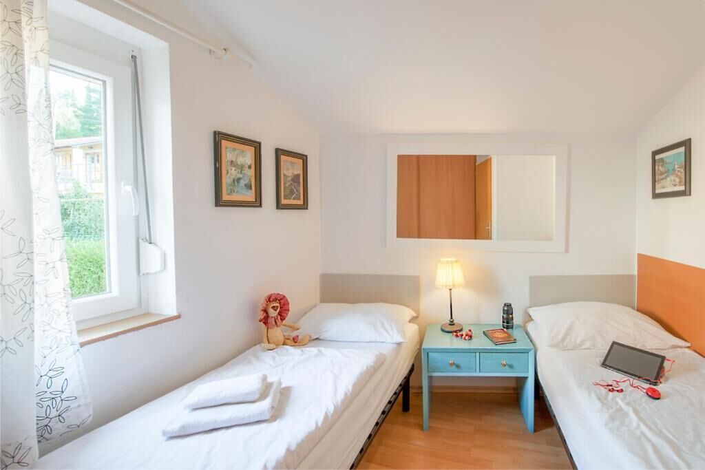 A bedroom with two single beds, a nightstand with a lamp, and a window with a curtain.