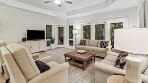 A spacious living room with a ceiling fan, a television, and a large window with a view of trees.