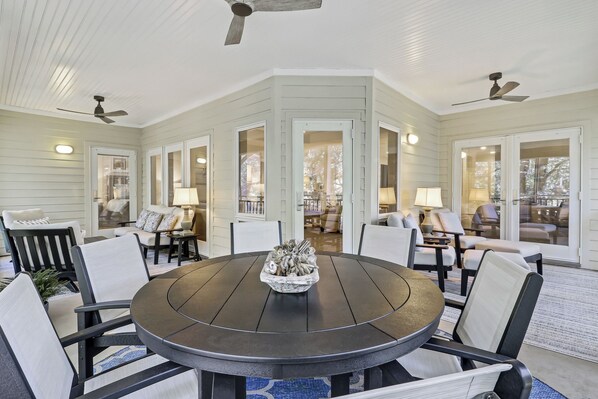 A covered patio area with a round table and chairs, a ceiling fan, and a view into the house.