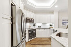 A modern kitchen with white cabinetry, stainless steel appliances, and a wooden floor.
