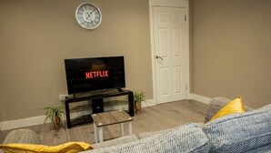 Un salon avec un téléviseur affichant le logo « NETFLIX », une porte blanche et une horloge au mur.