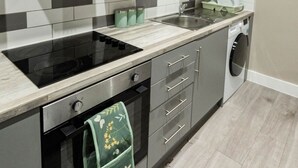 Une cuisine compacte dotée d’une cuisinière, d’un four et d’un micro-ondes intégrés, de placards gris et d’un lave-linge.