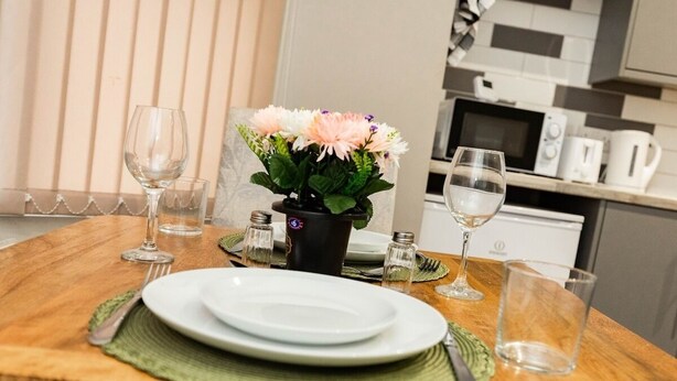 Une table à manger dressée avec des assiettes, des couverts et des verres, et un vase de fleurs placé au centre.