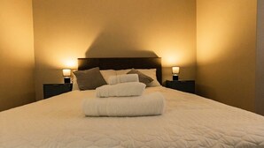 Un lit bien fait, recouvert d’une courtepointe, avec deux oreillers et une serviette pliée posée sur le dessus. De chaque côté du lit, on trouve une table de chevet avec une lampe.