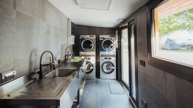 Un lavadero moderno con dos lavadoras apiladas, un lavamanos de acero inoxidable y una ventana con vistas al exterior.