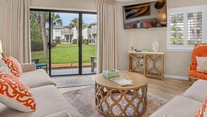 A living room with a large sliding glass door leading to a garden, a ceiling fan, and a flat-screen TV mounted on the wall. - Crystal Cove 28A-Walk to Beach-Sleeps 6 (Miramar Beach)