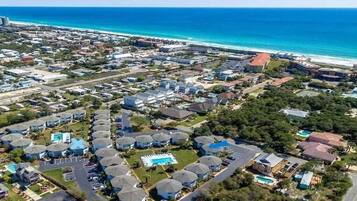 An aerial view of a coastal residential area with houses, a swimming pool, and a beach in the background.