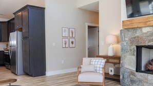 A modern living room with a sofa, a coffee table, a fireplace, and a kitchen area with dark cabinets and a refrigerator.