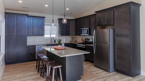 A modern kitchen with dark cabinets, stainless steel appliances, and a central island with stools.