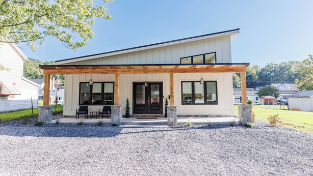 A modern two-story house with a covered porch, large windows, and a stone pathway leading to the entrance.
