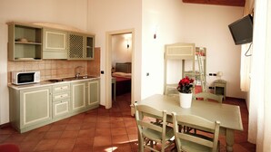 A compact kitchen with a microwave, sink, and wooden cabinets. There is a dining area with a table and chairs, and a small TV mounted on the wall. - APARTMENT A FEW KILOMETERS FROM THE BEACH (Sala)