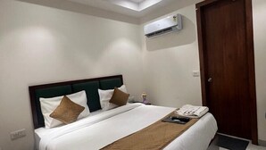 A hotel room with a bed, a ceiling fan, an air conditioning unit, and a wooden door. - HOTEL IVORY INN (New Delhi)