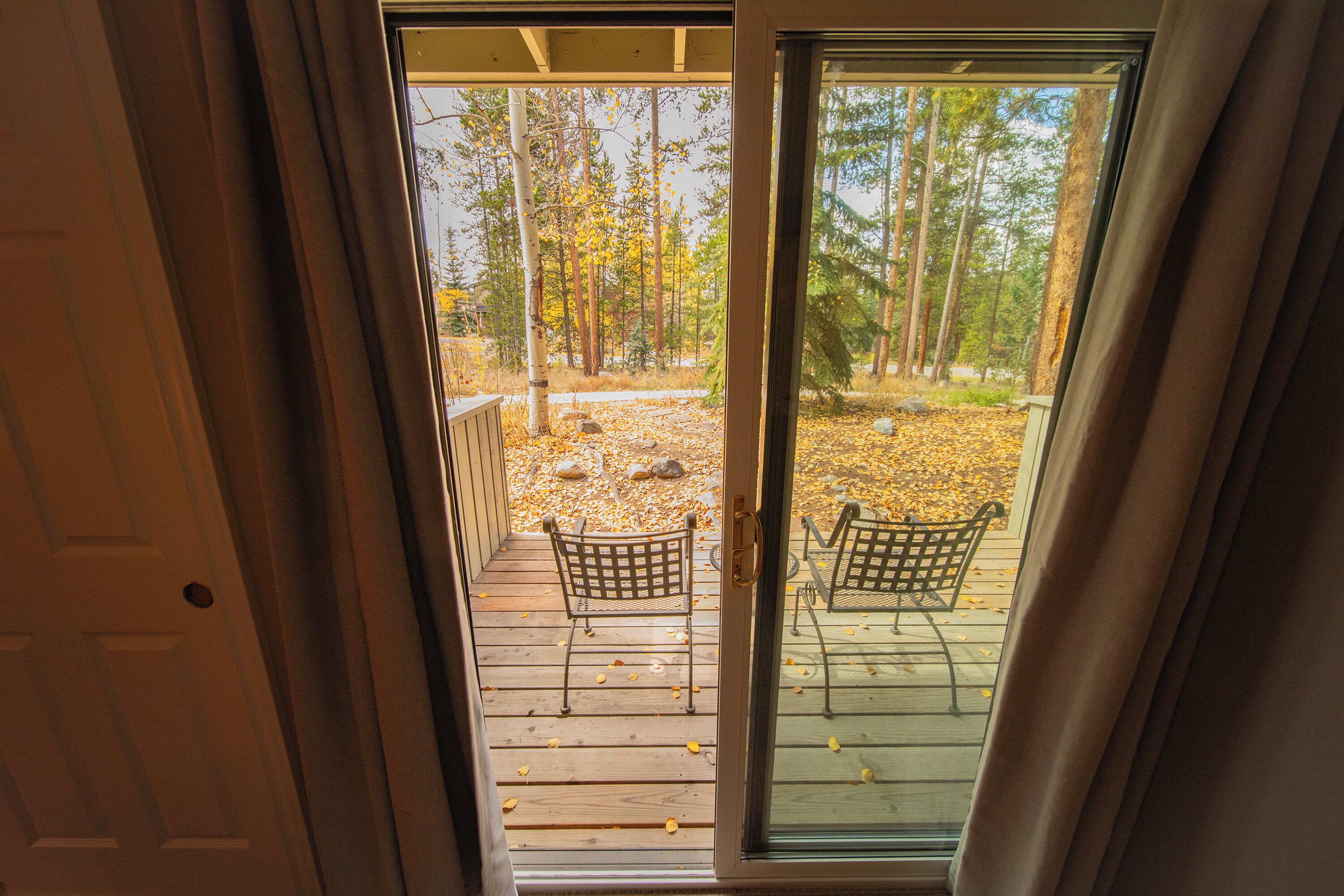 A wooden deck with two metal chairs, a glass door leading to a forested area.