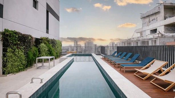 Un espace piscine aménagé sur le toit, offrant une vue sur le panorama urbain, avec des chaises longues et une petite table.