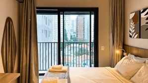 Une chambre d’hôtel avec un lit, une table de chevet, une fenêtre avec des rideaux et une vue sur les bâtiments environnants.