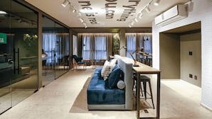 Un salon moderne avec un canapé, une table basse et un bureau avec une lampe. Il y a des rideaux aux fenêtres et un climatiseur fixé au mur.