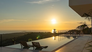 Una piscina a sfioro con due lettini, vista sul tramonto e cielo sereno.