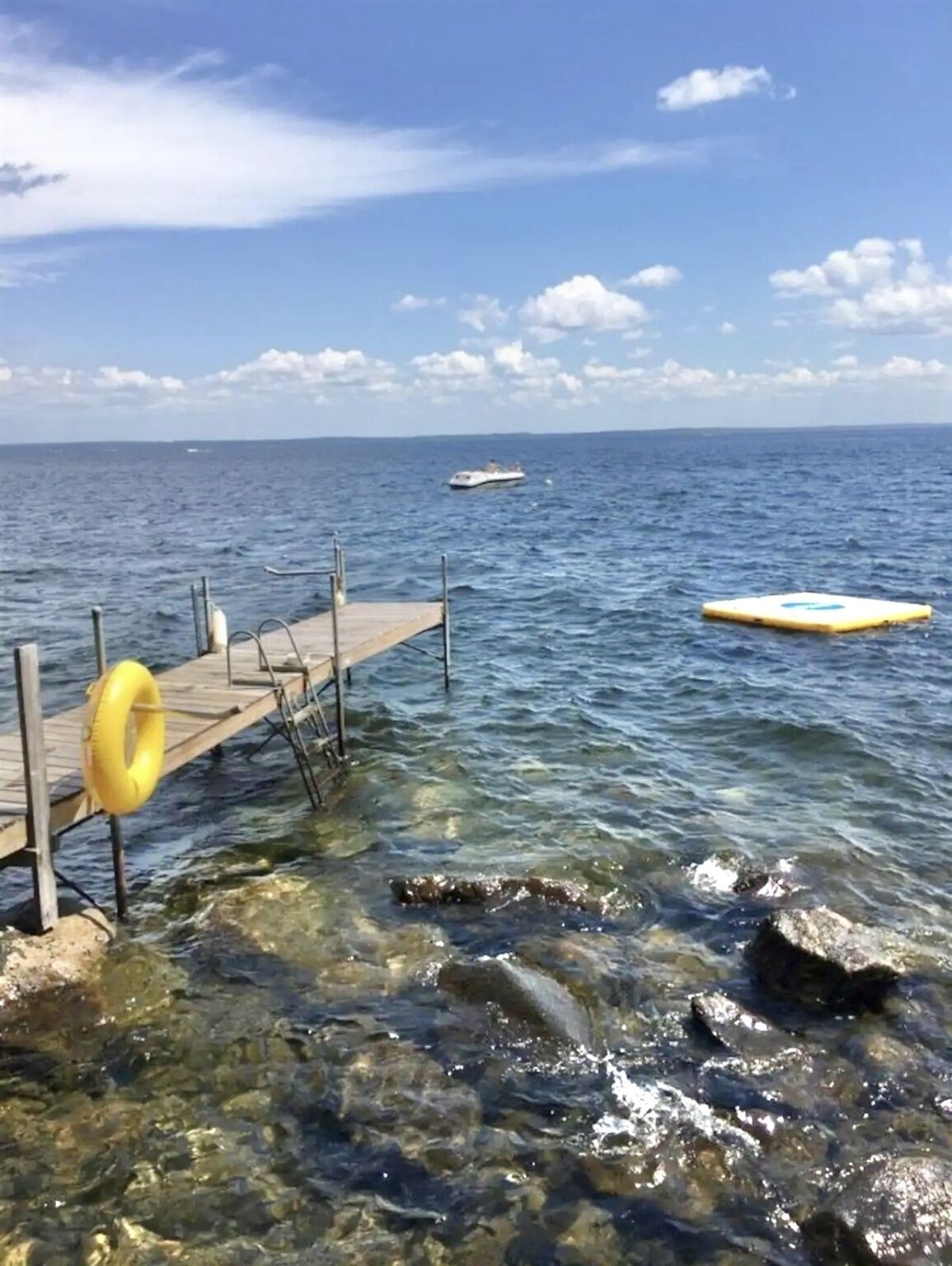 A pier extending into a clear blue sea with a boat in the distance and a yellow buoy in the water.