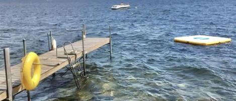 A pier extending into a clear blue sea with a boat in the distance and a yellow buoy in the water.